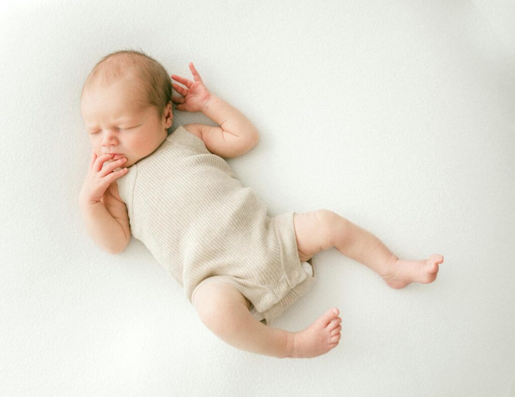 Baby in Beige Rompers Sleeping with a Finger in Mouth